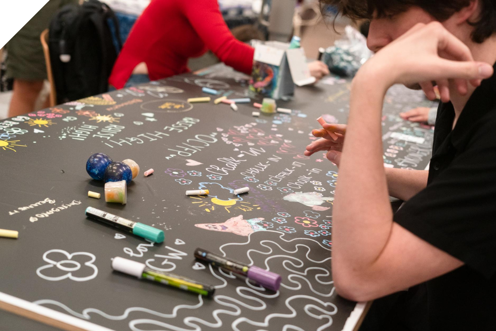 Students write on a table at GW Wellbeing's annual chalk-in event
