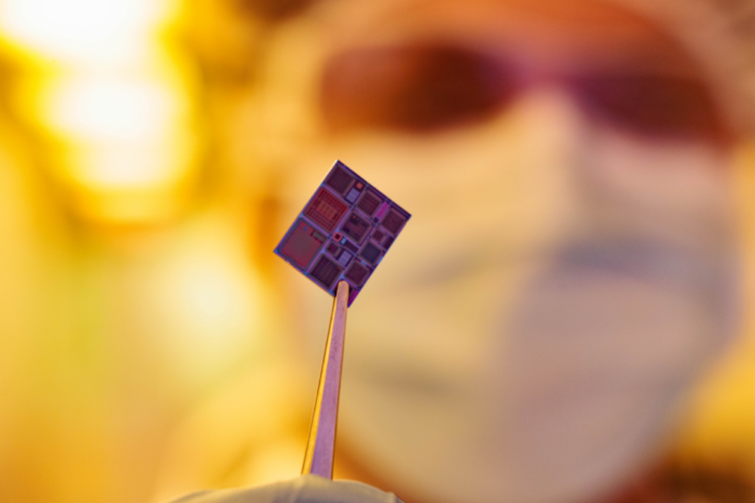 A scientist holds a microchip up with tweezers