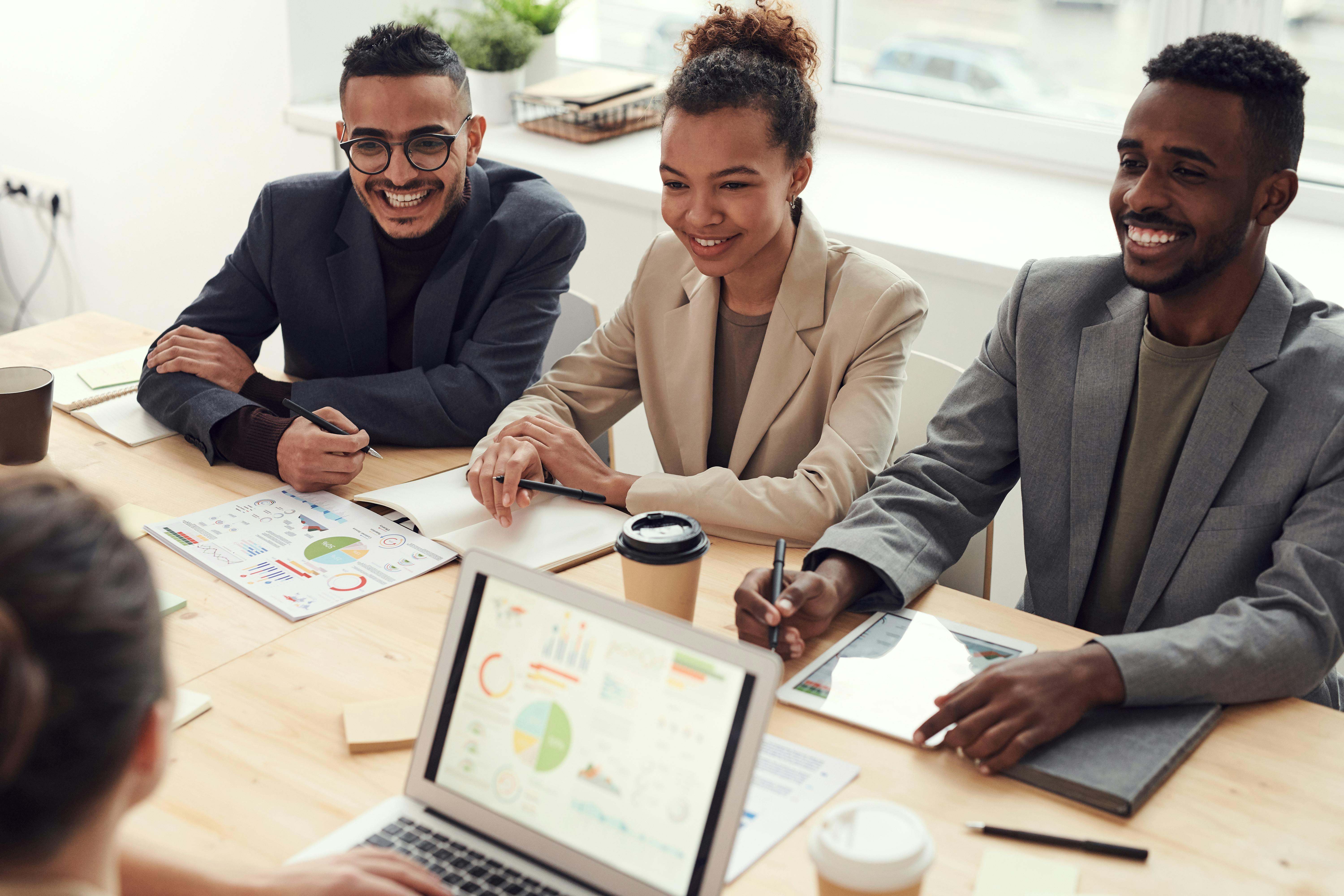 three smiling students sit across from a person using a laptop to display charts and graphs