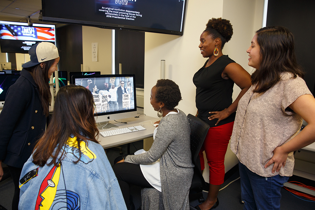 A group of students look at a computer monitor in the School of Media & Public Affairs